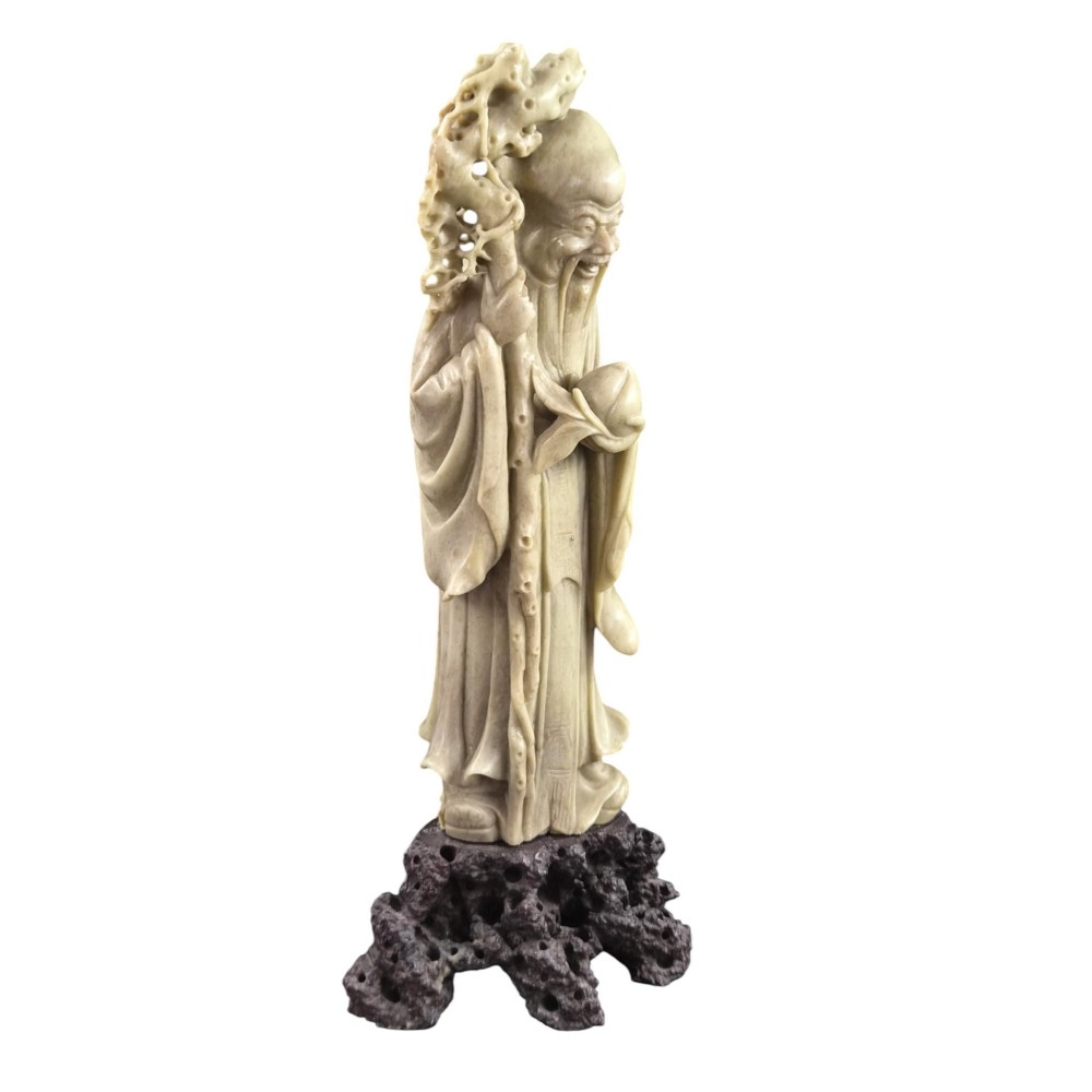 A late 19th-century carved pale soapstone figure of Shoulao holding a peach and staff, standing on a dark stone pierced rockwork base. View VI