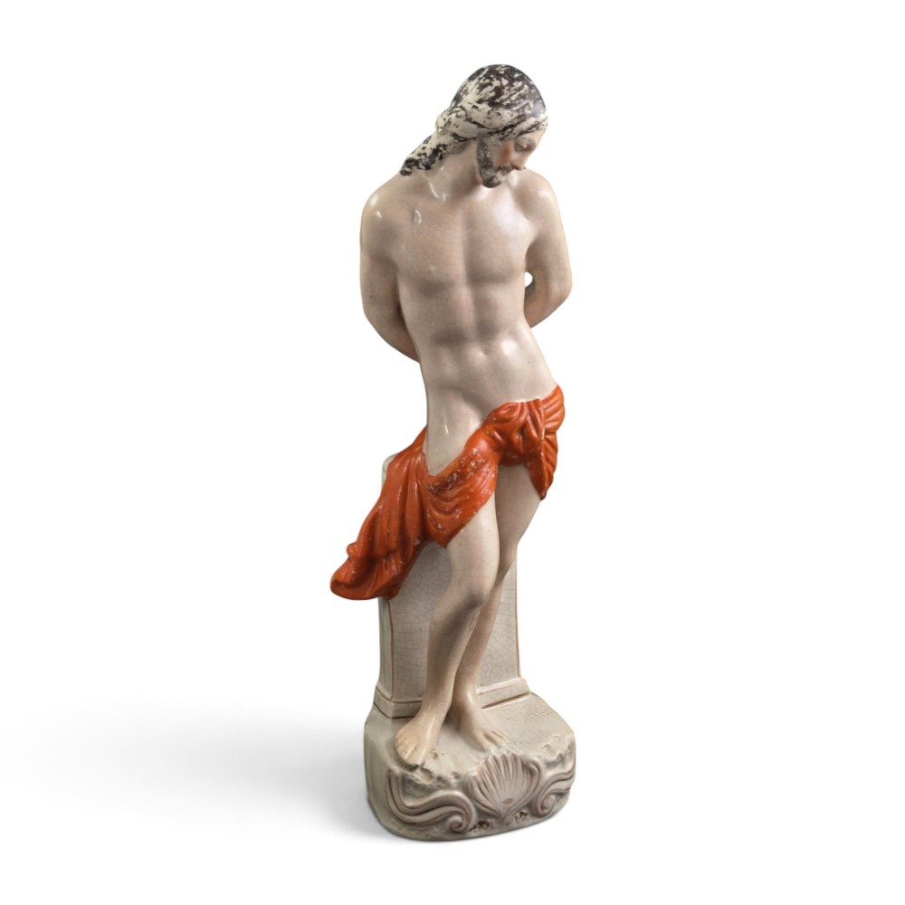 A Victorian earthenware figurine depicting Christ standing at a column draped in a terracotta-coloured cloth on a scrollwork base.