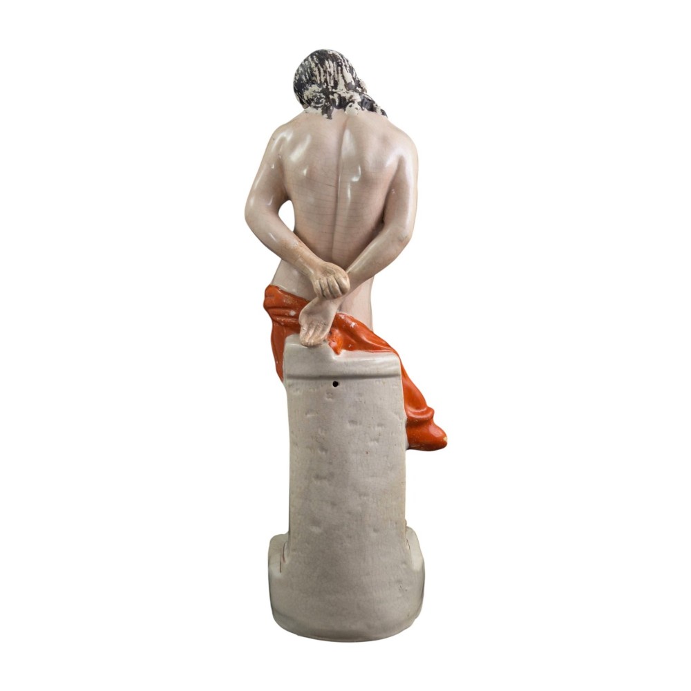 A Victorian earthenware figurine depicting Christ standing at a column draped in a terracotta-coloured cloth on a scrollwork base. View VII