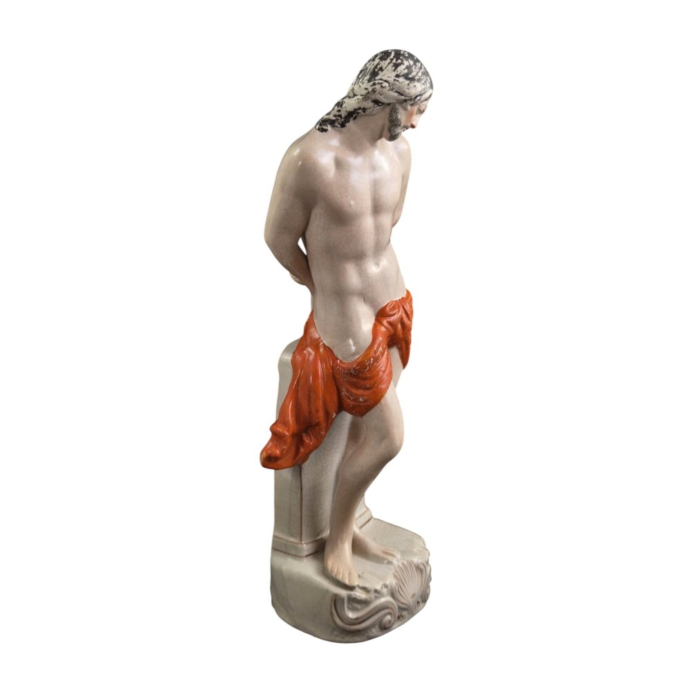 A Victorian earthenware figurine depicting Christ standing at a column draped in a terracotta-coloured cloth on a scrollwork base. View VIII