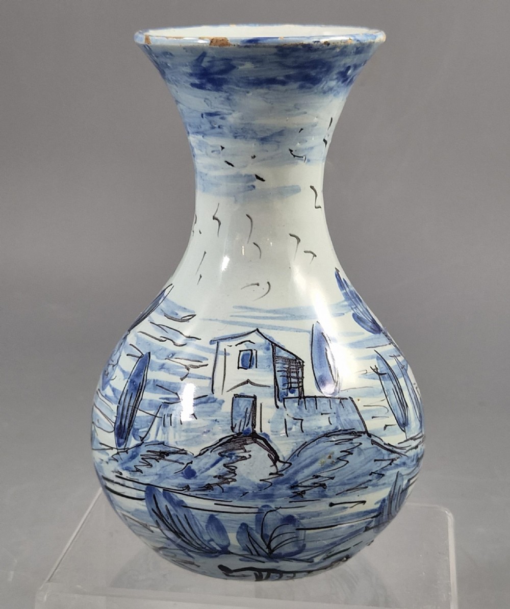 An antique bulbous blue and white maiolica ceramic vase decorated with a hand-painted architectural landscape scene and a flared rim.