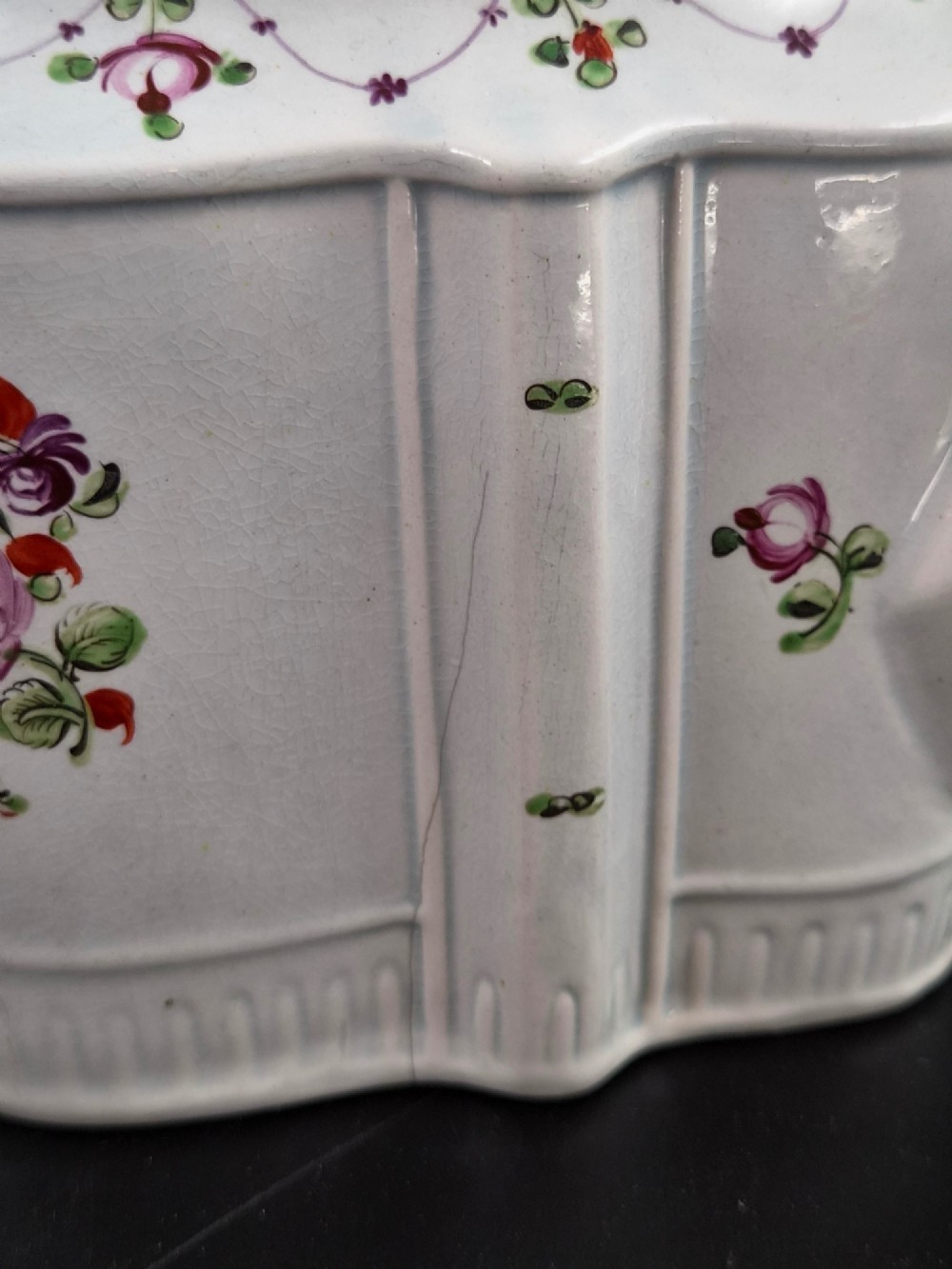 An off-white earthenware commode-shaped teapot decorated with hand-painted floral sprays, red borders, and a seated widow finial on the lid. View XIII