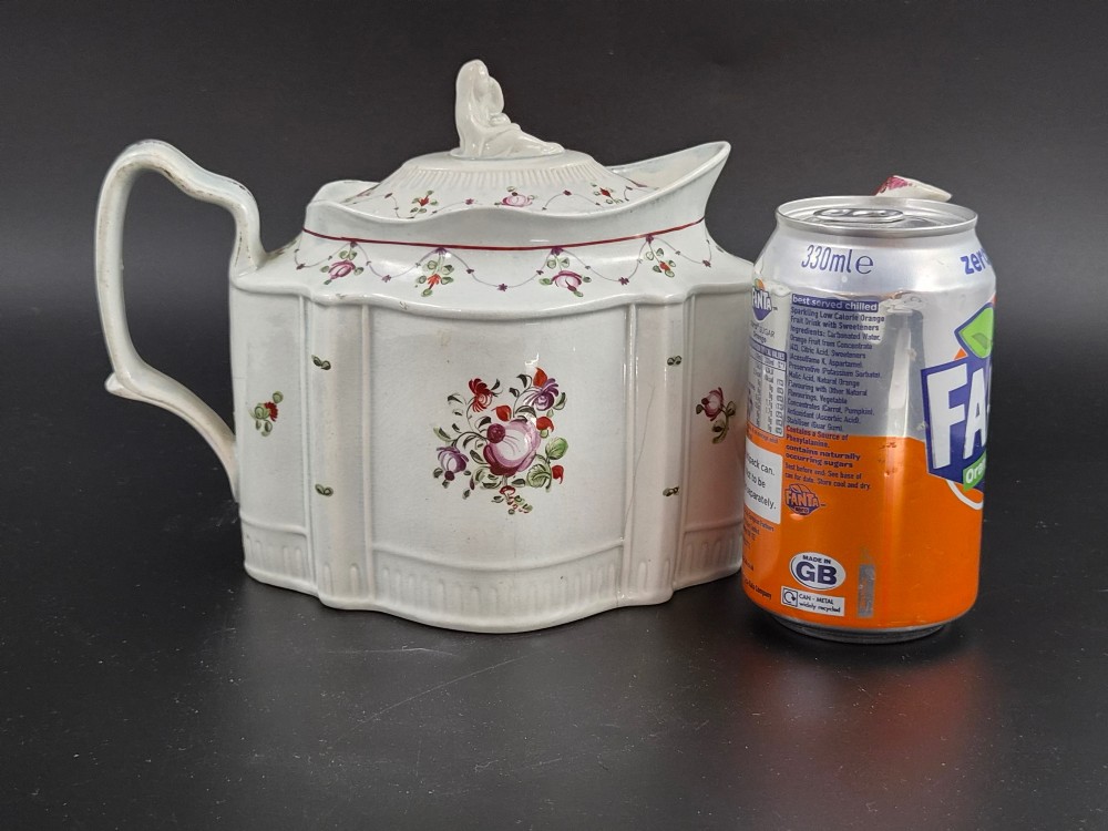 An off-white earthenware commode-shaped teapot decorated with hand-painted floral sprays, red borders, and a seated widow finial on the lid. View XIV