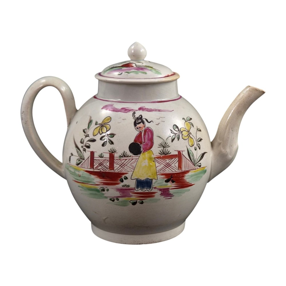 An 18th-century creamware teapot featuring hand-painted polychrome Chinoiserie figures on a cream glaze background with a curved spout and loop handle. View IV