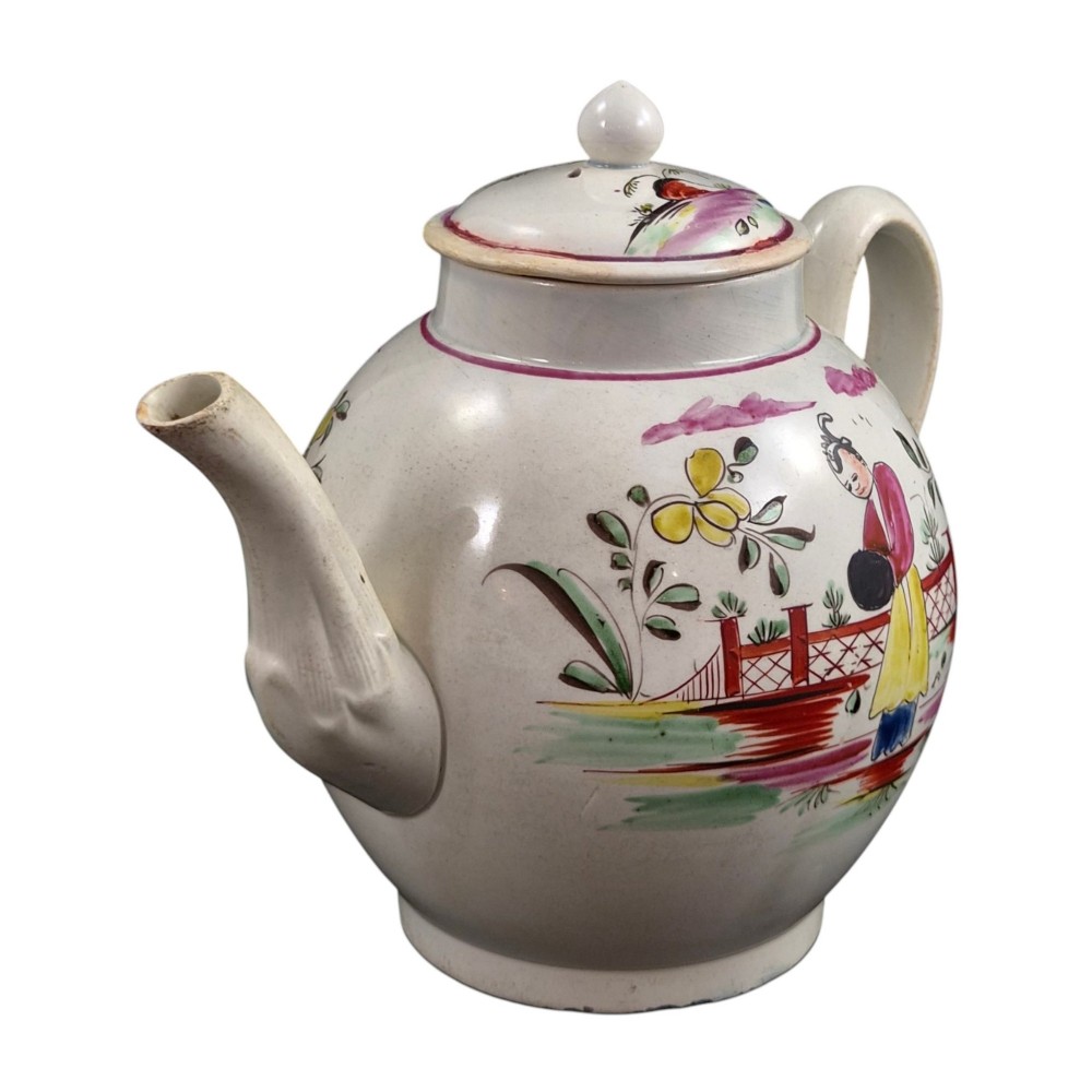 An 18th-century creamware teapot featuring hand-painted polychrome Chinoiserie figures on a cream glaze background with a curved spout and loop handle. View VI