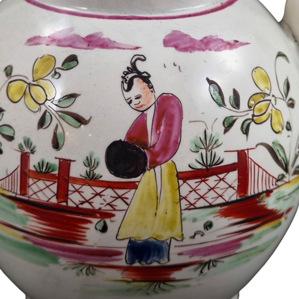 An 18th-century creamware teapot featuring hand-painted polychrome Chinoiserie figures on a cream glaze background with a curved spout and loop handle. View VII