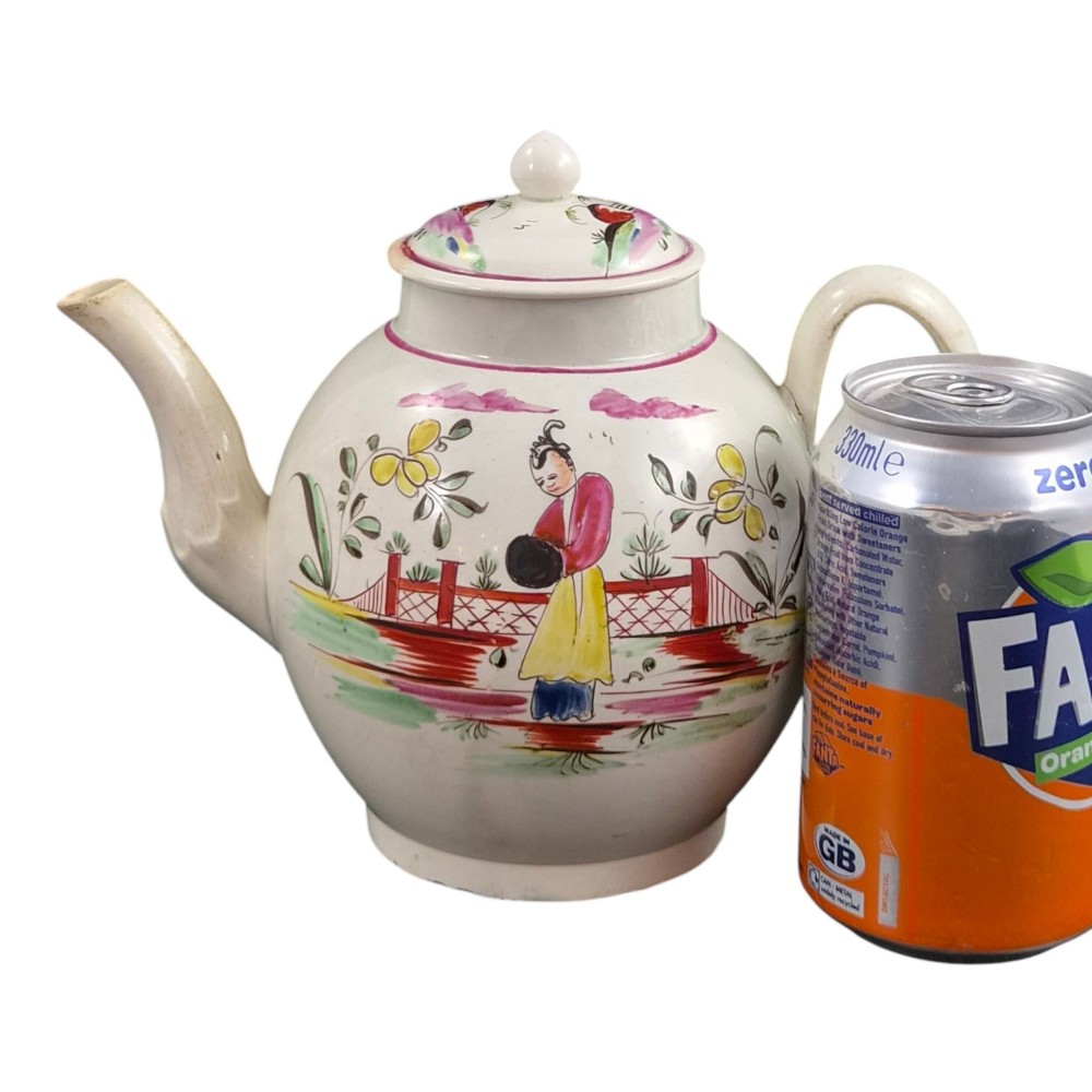 An 18th-century creamware teapot featuring hand-painted polychrome Chinoiserie figures on a cream glaze background with a curved spout and loop handle. View XV