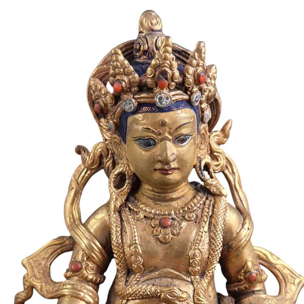 A gilt bronze figure of the deity Jambhala crowned and adorned with jewellery, seated upon a snow lion atop an oval lotus pedestal base with red and blue painted accents. View II