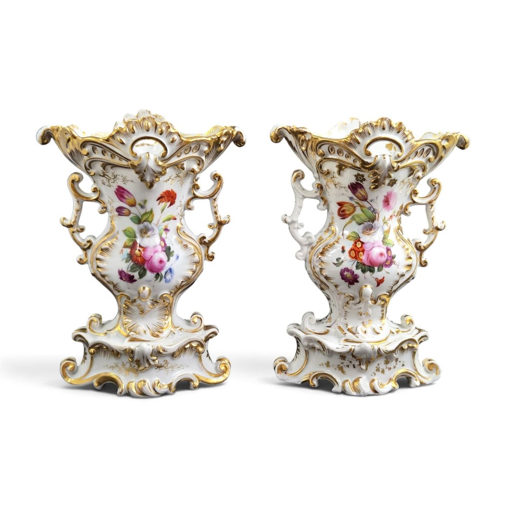 A pair of ornate white and gilded porcelain Rococo vases featuring hand-painted floral bouquets, pierced rims, and scroll handles.