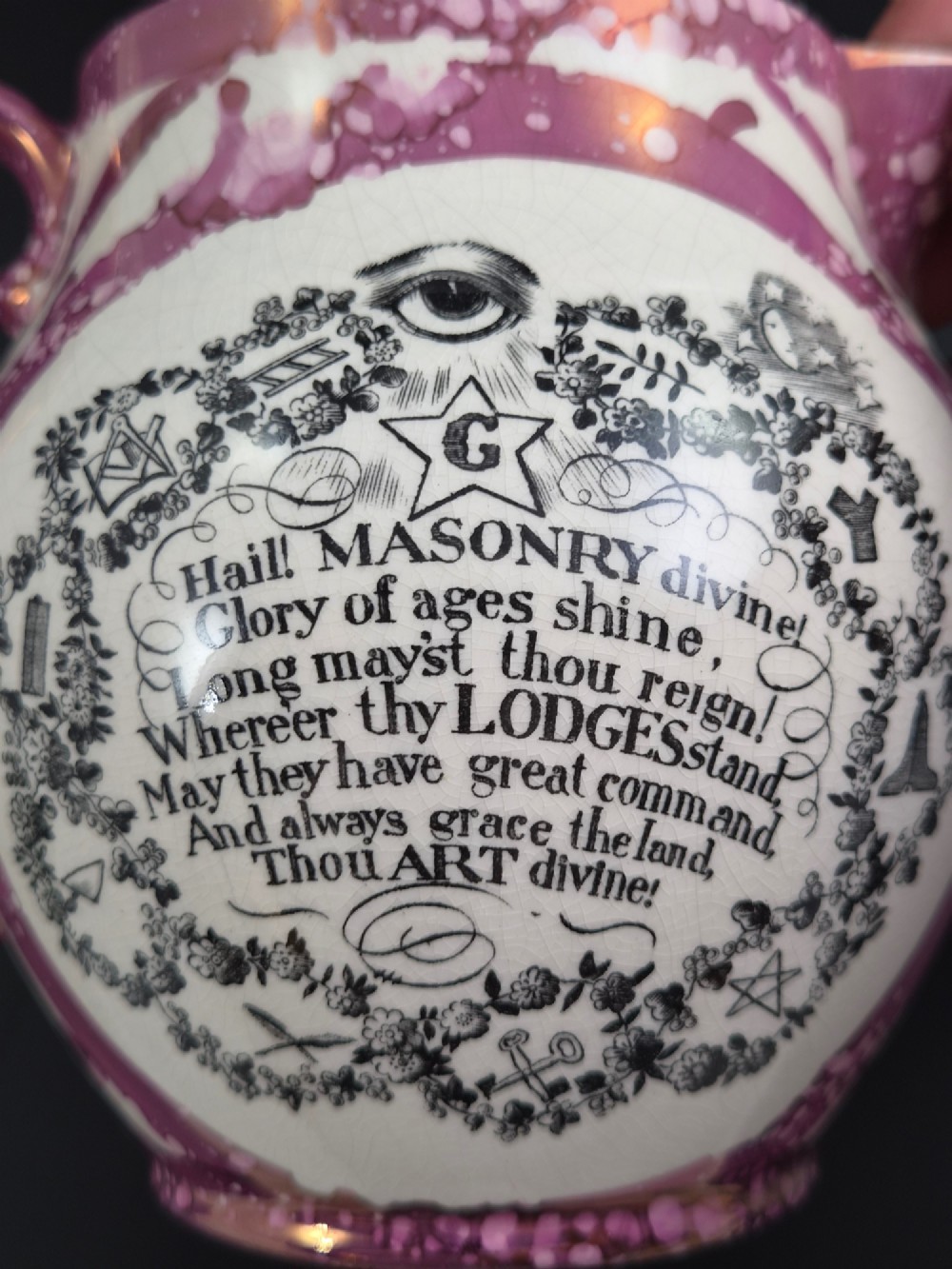 An English earthenware jug featuring pink splash lustre glaze trim and a central black transfer-printed Masonic emblem. View X