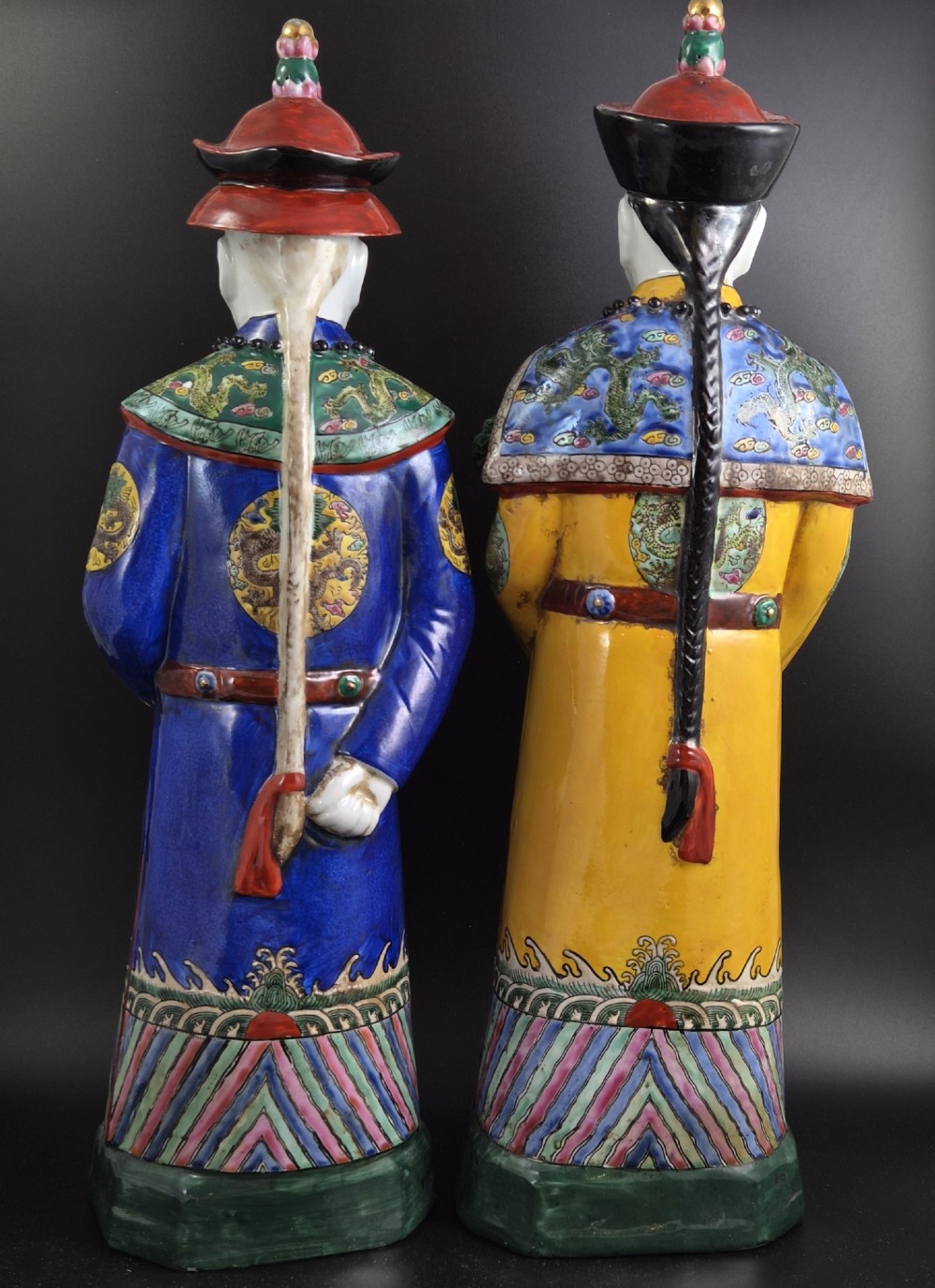A pair of tall Chinese porcelain figures wearing traditional Qing Dynasty imperial robes in bright yellow and royal blue, adorned with dragon roundels and court beads. View III