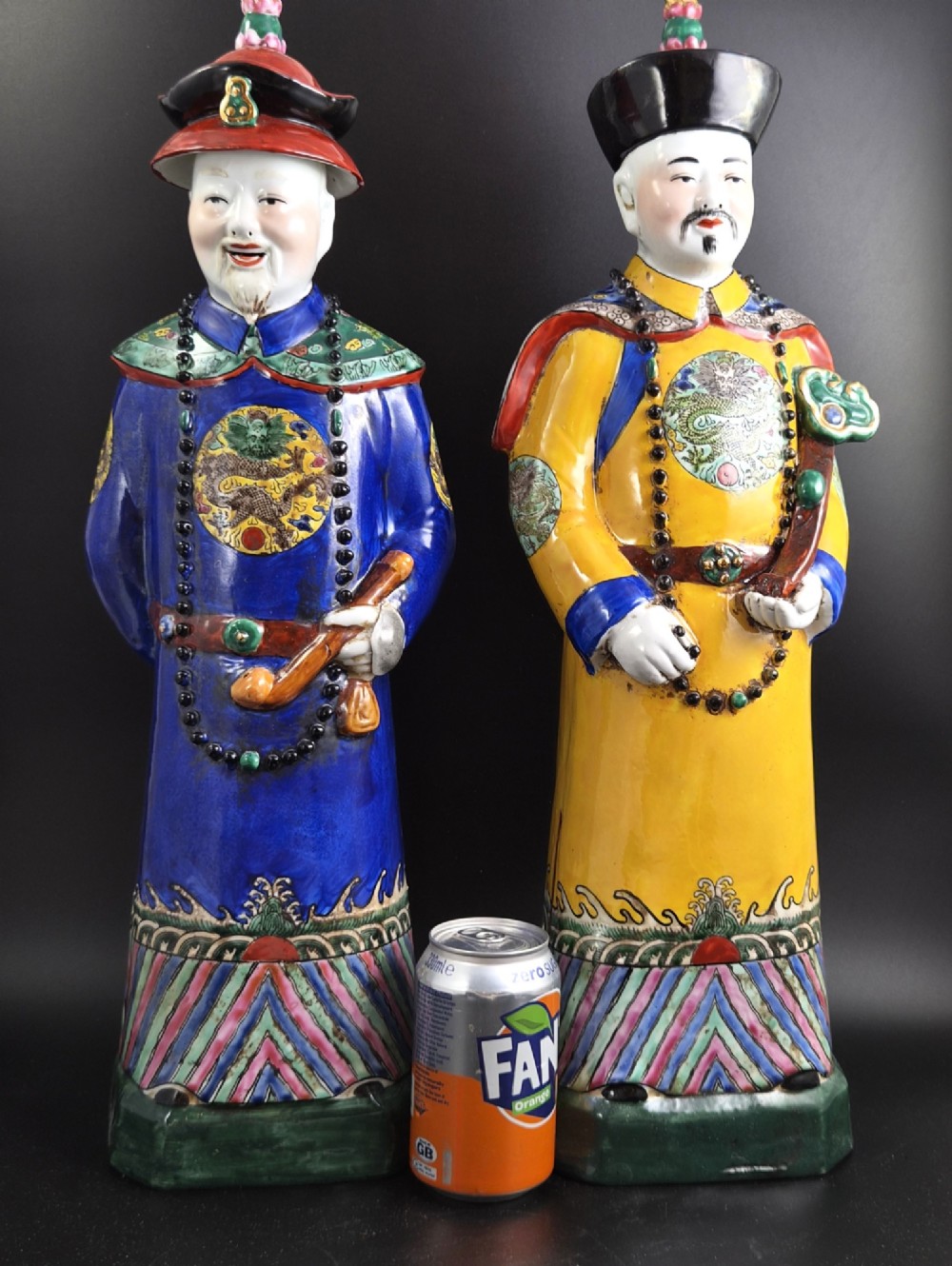 A pair of tall Chinese porcelain figures wearing traditional Qing Dynasty imperial robes in bright yellow and royal blue, adorned with dragon roundels and court beads. View V