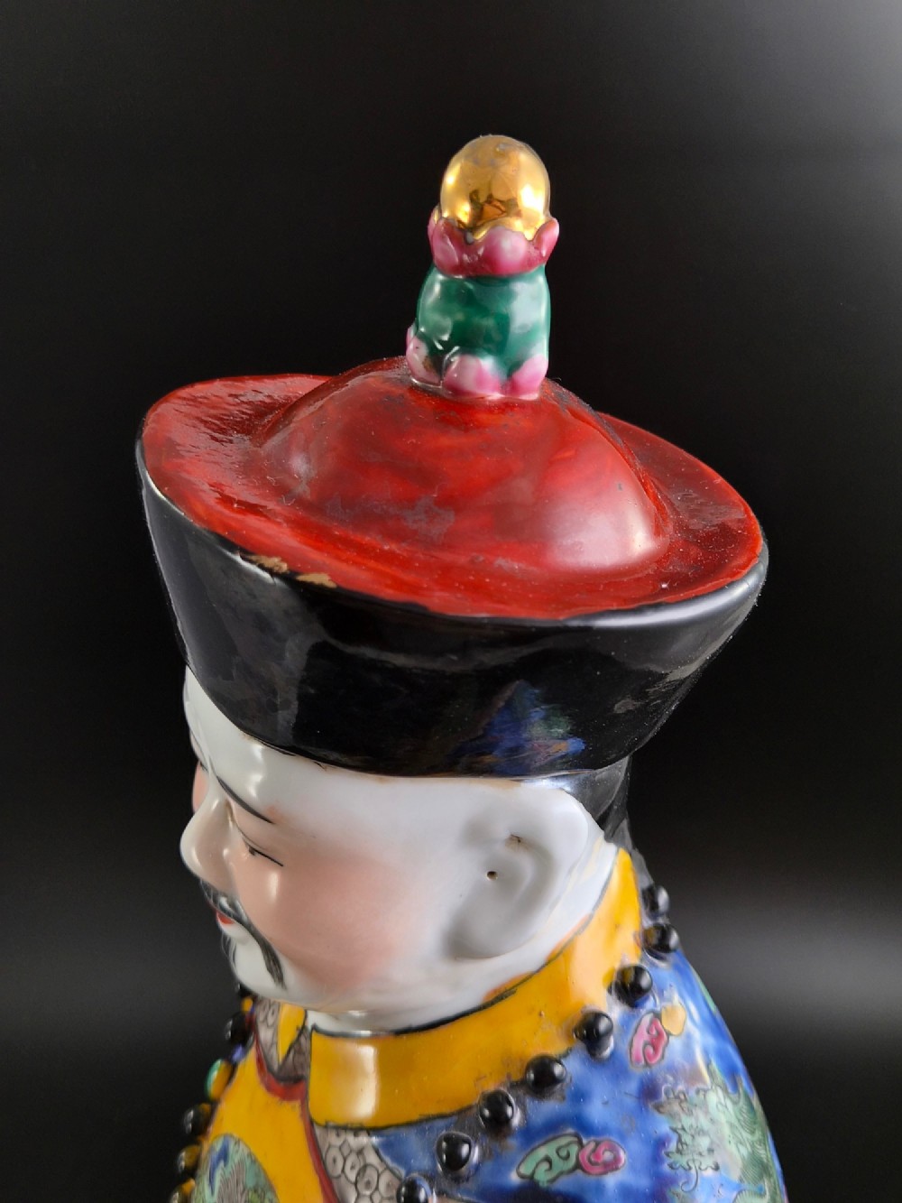 A pair of tall Chinese porcelain figures wearing traditional Qing Dynasty imperial robes in bright yellow and royal blue, adorned with dragon roundels and court beads. View IX