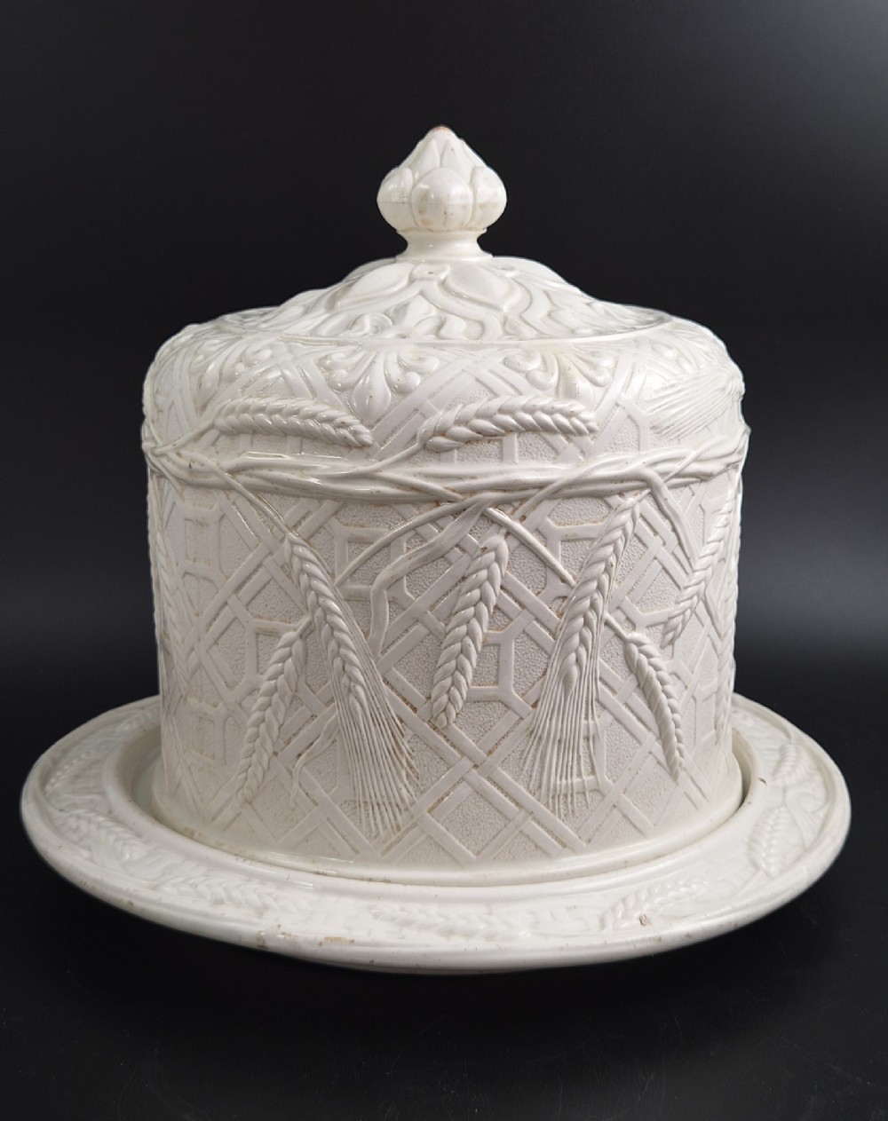 An off-white Victorian ironstone cheese dome and matching circular stand with molded relief lattice work and wheat sheaf motifs.