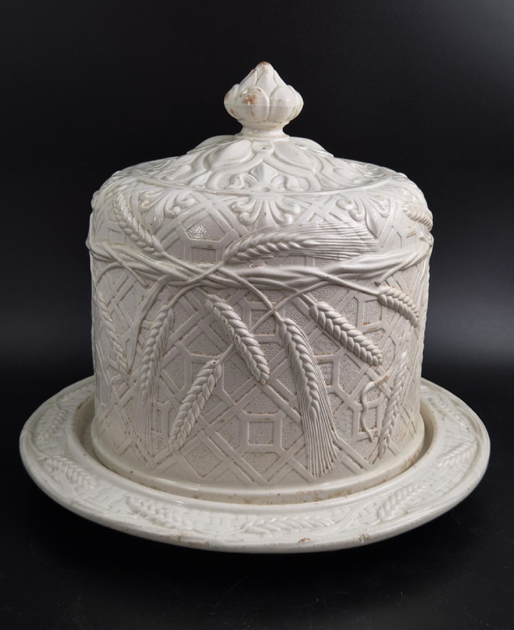 An off-white Victorian ironstone cheese dome and matching circular stand with molded relief lattice work and wheat sheaf motifs. View V
