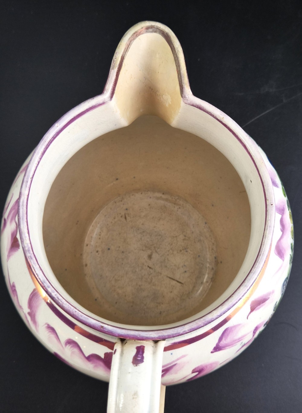 An antique cream earthenware jug decorated with pink splash lustre glaze and a central transfer print depicting the Iron Bridge over the Wear. View VII