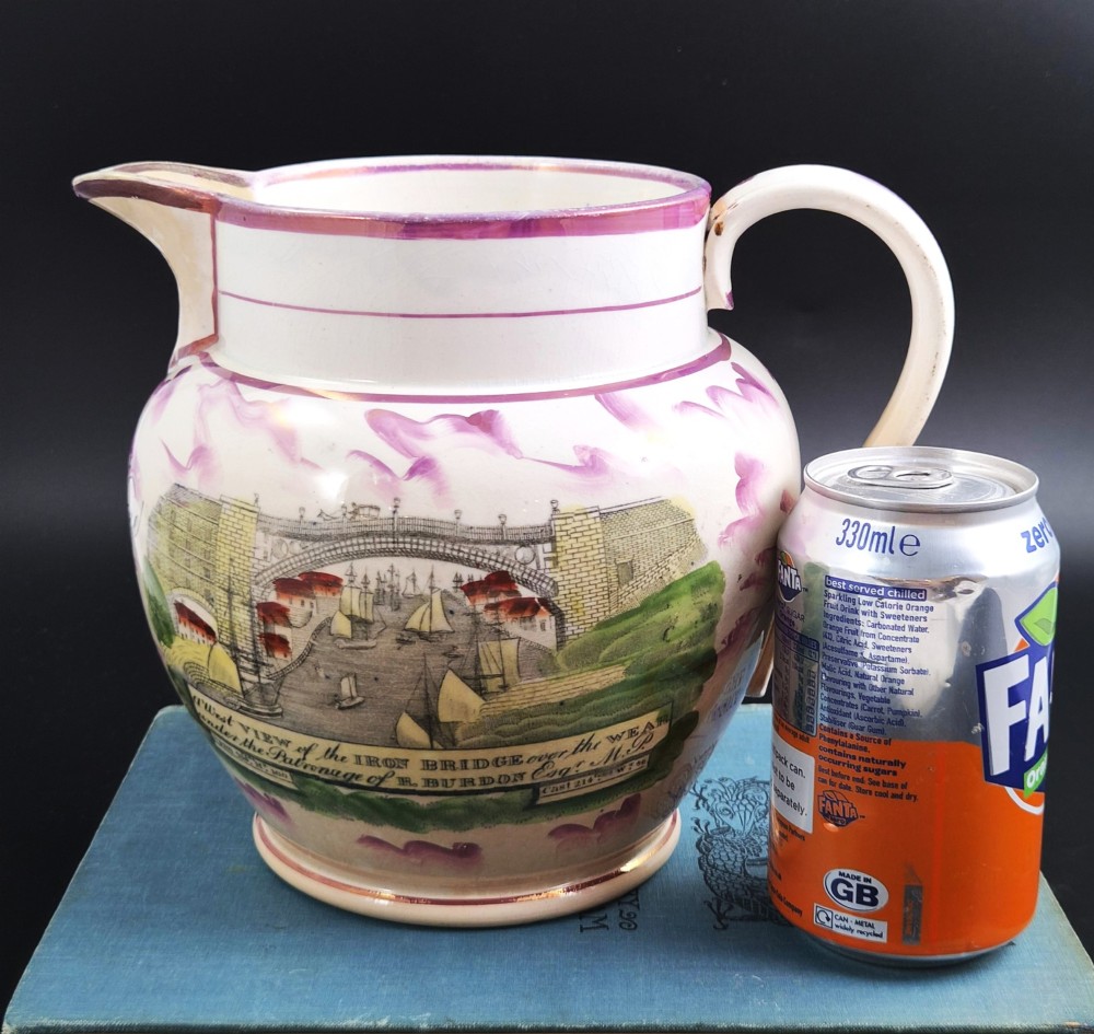 An antique cream earthenware jug decorated with pink splash lustre glaze and a central transfer print depicting the Iron Bridge over the Wear. View IX