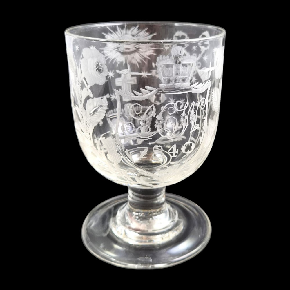 A clear lead-glass rummer featuring detailed wheel-engraved fraternal symbols, including a central cross, all-seeing eye, crowns, and floral garlands, resting on a short stem and circular foot. View IV