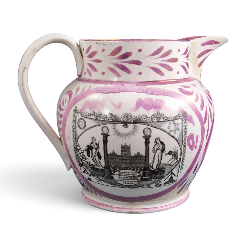 An antique white earthenware jug decorated with pink metallic lustre foliage borders and a black transfer-printed Masonic emblem featuring twin columns and symbolic motifs.