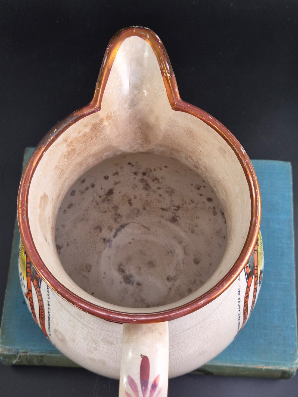 A cream earthenware jug featuring hand-painted floral motifs, copper lustre trim, and a printed Orange Order emblematic coat of arms with religious and fraternal symbols. View V