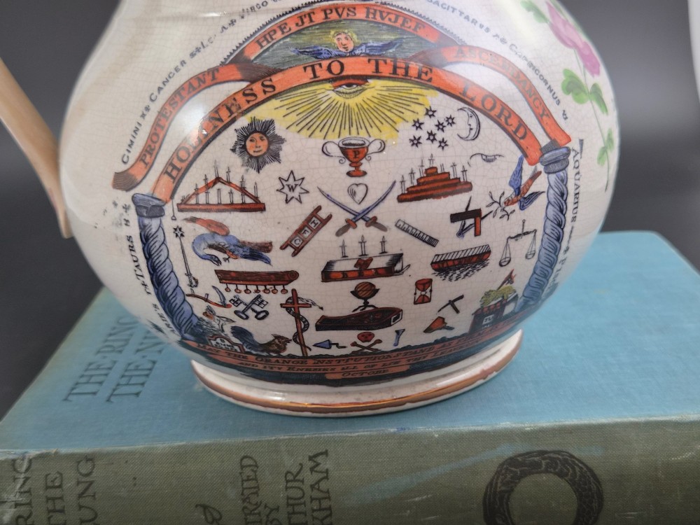 A cream earthenware jug featuring hand-painted floral motifs, copper lustre trim, and a printed Orange Order emblematic coat of arms with religious and fraternal symbols. View IX
