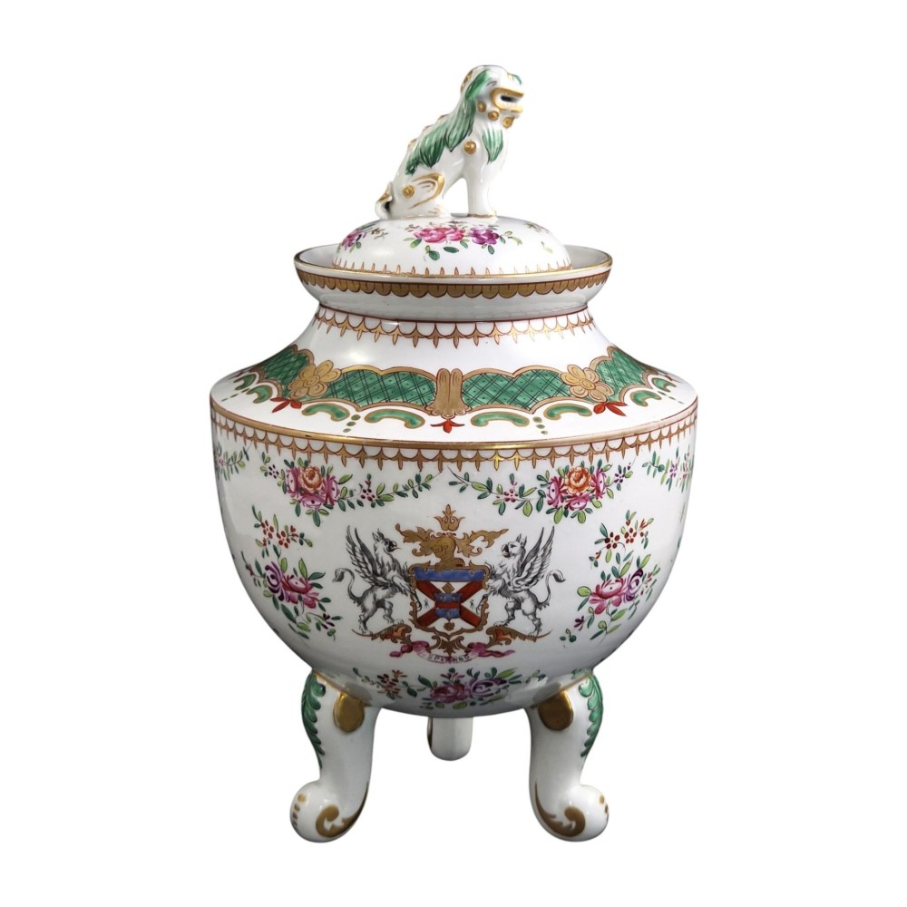 A white hard-paste porcelain covered jar on three cabriole legs, decorated with floral enamel sprays, an armorial crest, green lattice borders, and topped with a foo dog lid finial. View II