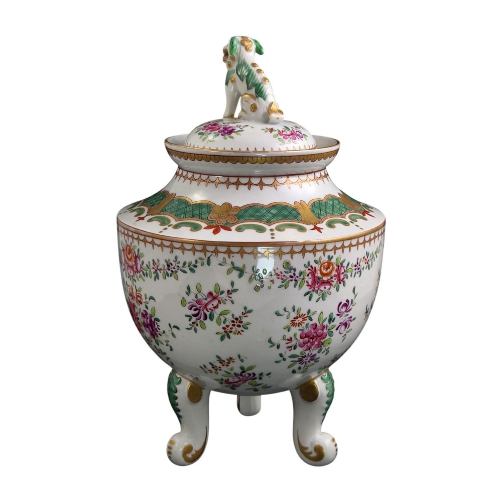 A white hard-paste porcelain covered jar on three cabriole legs, decorated with floral enamel sprays, an armorial crest, green lattice borders, and topped with a foo dog lid finial. View V