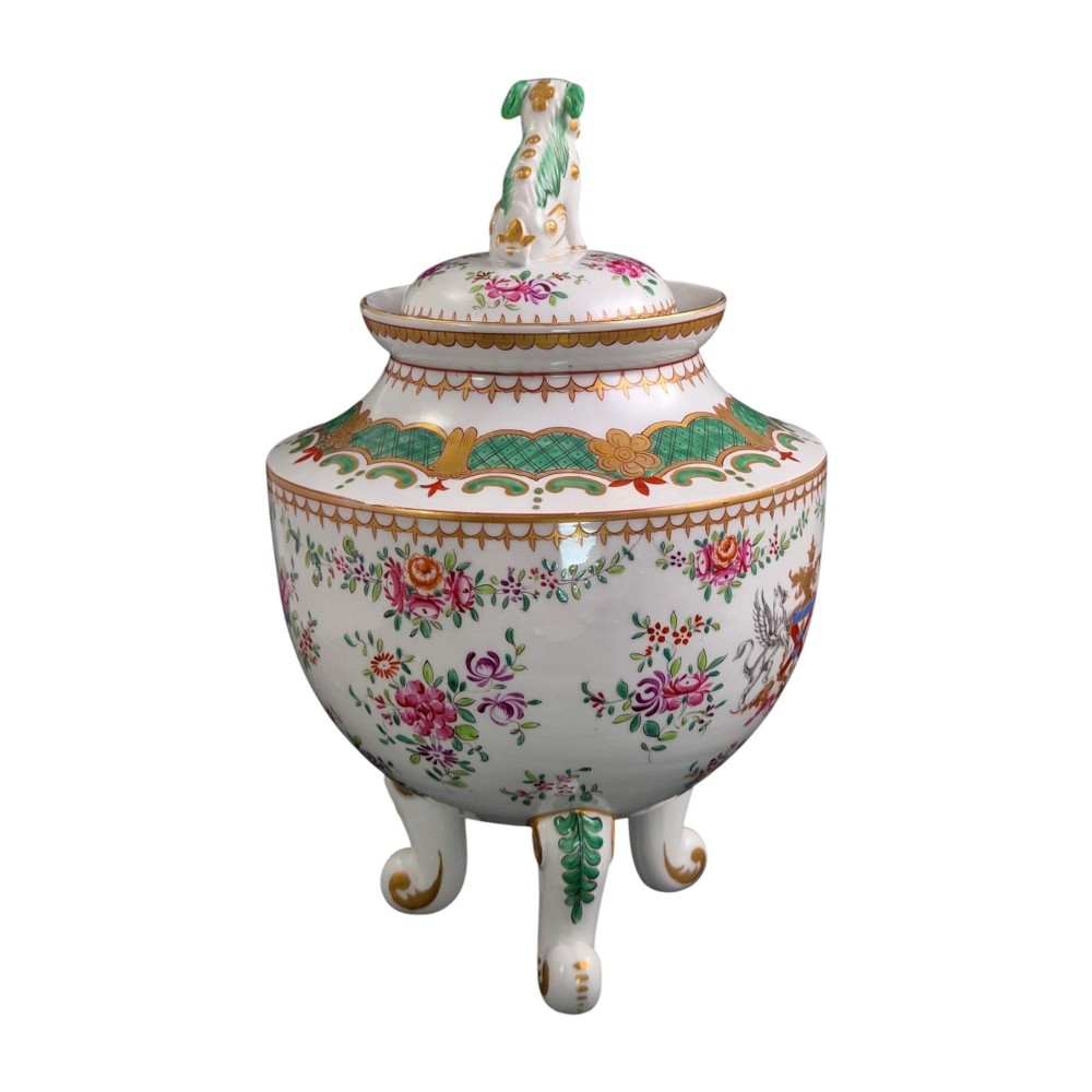 A white hard-paste porcelain covered jar on three cabriole legs, decorated with floral enamel sprays, an armorial crest, green lattice borders, and topped with a foo dog lid finial. View VI