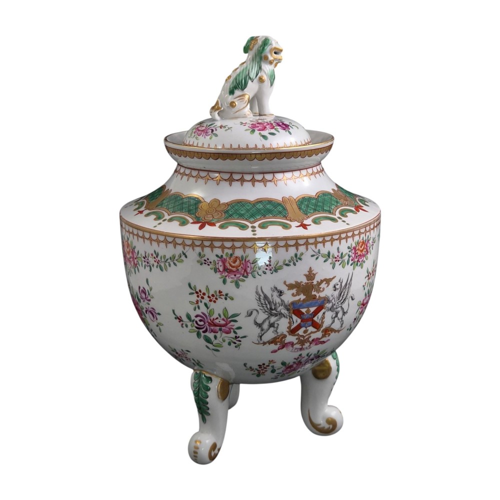 A white hard-paste porcelain covered jar on three cabriole legs, decorated with floral enamel sprays, an armorial crest, green lattice borders, and topped with a foo dog lid finial. View VII