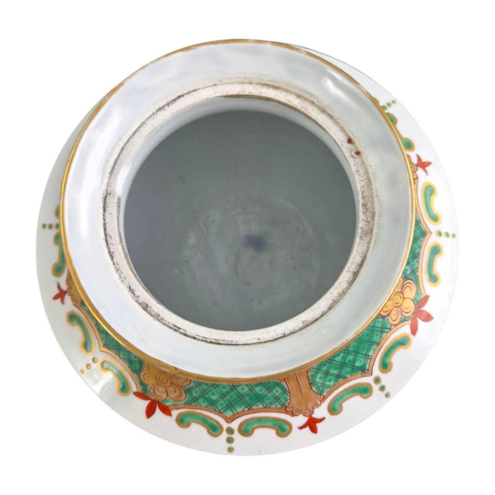 A white hard-paste porcelain covered jar on three cabriole legs, decorated with floral enamel sprays, an armorial crest, green lattice borders, and topped with a foo dog lid finial. View X