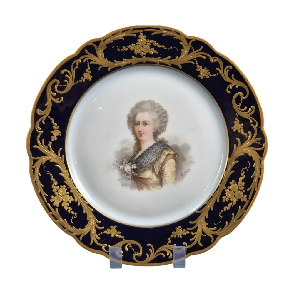 A circular porcelain cabinet plate featuring a central hand-painted portrait of a woman framed by a deep cobalt blue rim with gold scrollwork. View VI
