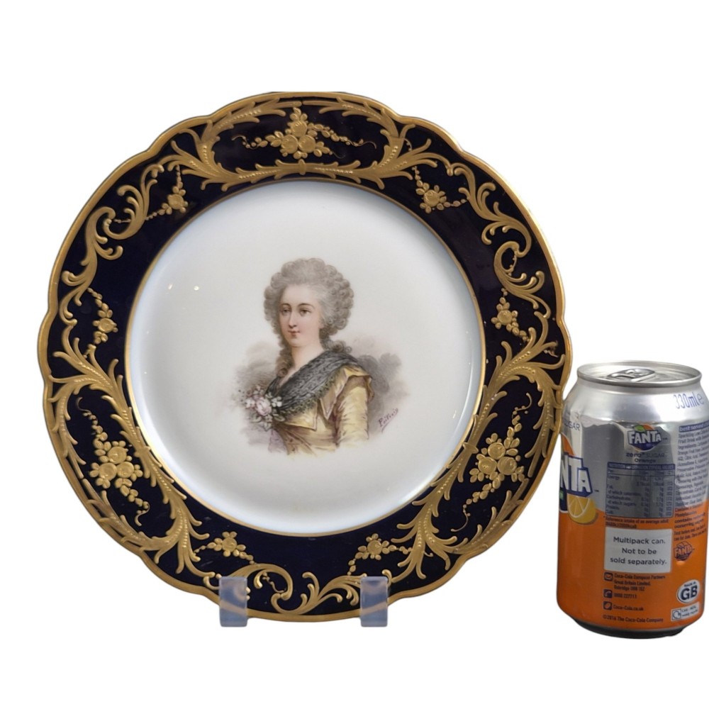 A circular porcelain cabinet plate featuring a central hand-painted portrait of a woman framed by a deep cobalt blue rim with gold scrollwork. View VII