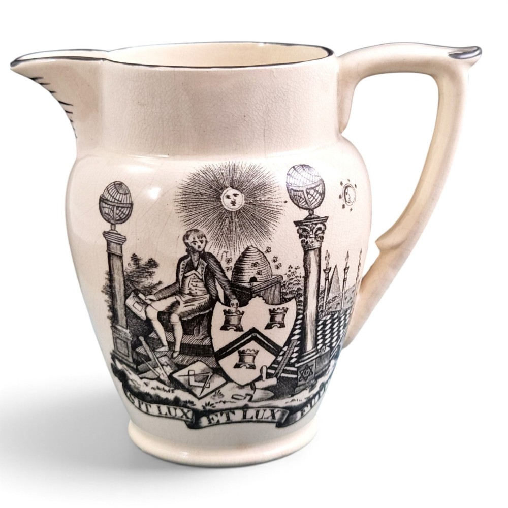 A creamware ceramic jug featuring detailed black transfer prints of Masonic emblems, including classical columns, a beehive, and a coat of arms.