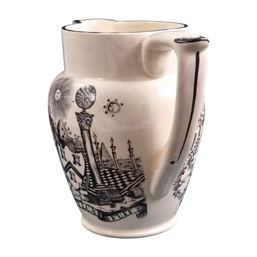 A creamware ceramic jug featuring detailed black transfer prints of Masonic emblems, including classical columns, a beehive, and a coat of arms. View II