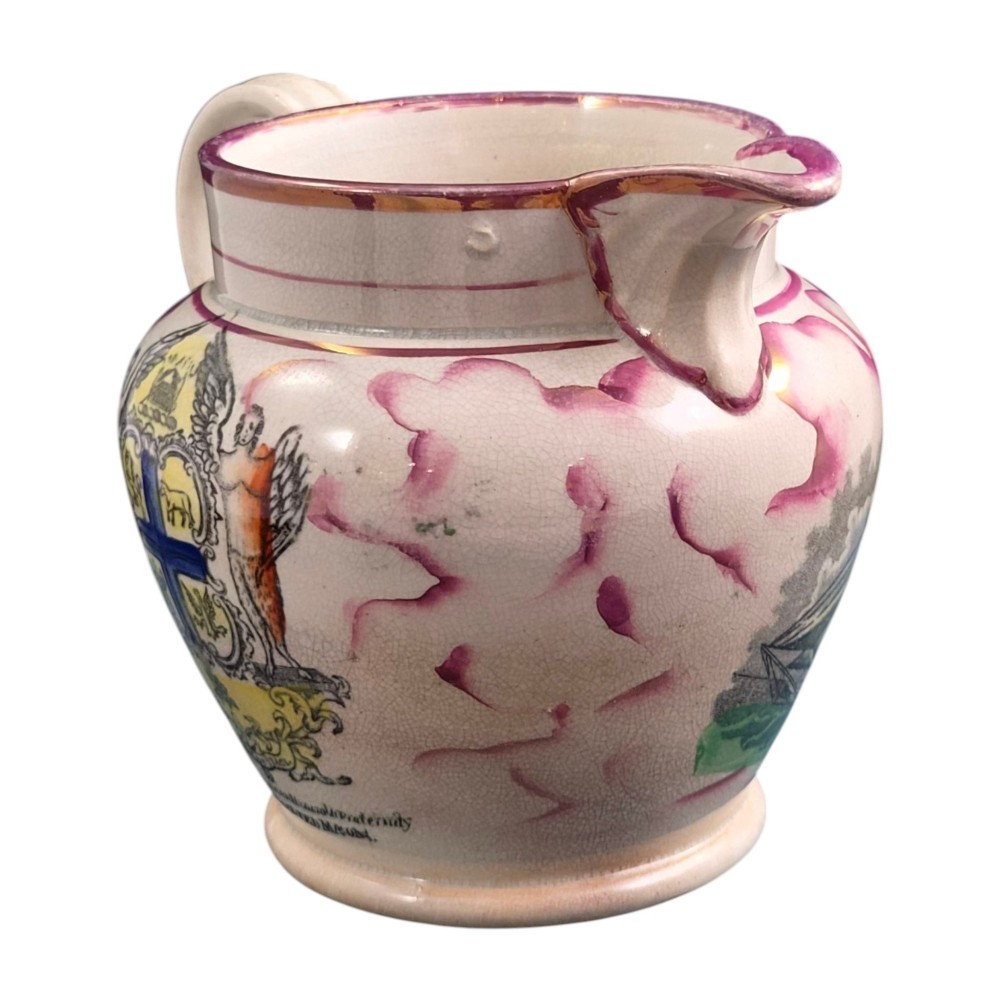 An antique cream earthenware jug featuring pink splash lustre decoration and a hand-coloured transfer print of Masonic coats of arms. View II