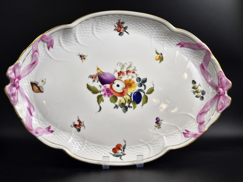 An oval white porcelain tray featuring hand-painted fruit and insect motifs, moulded basketweave border, pink painted ribbon handles, and a gilded rim.
