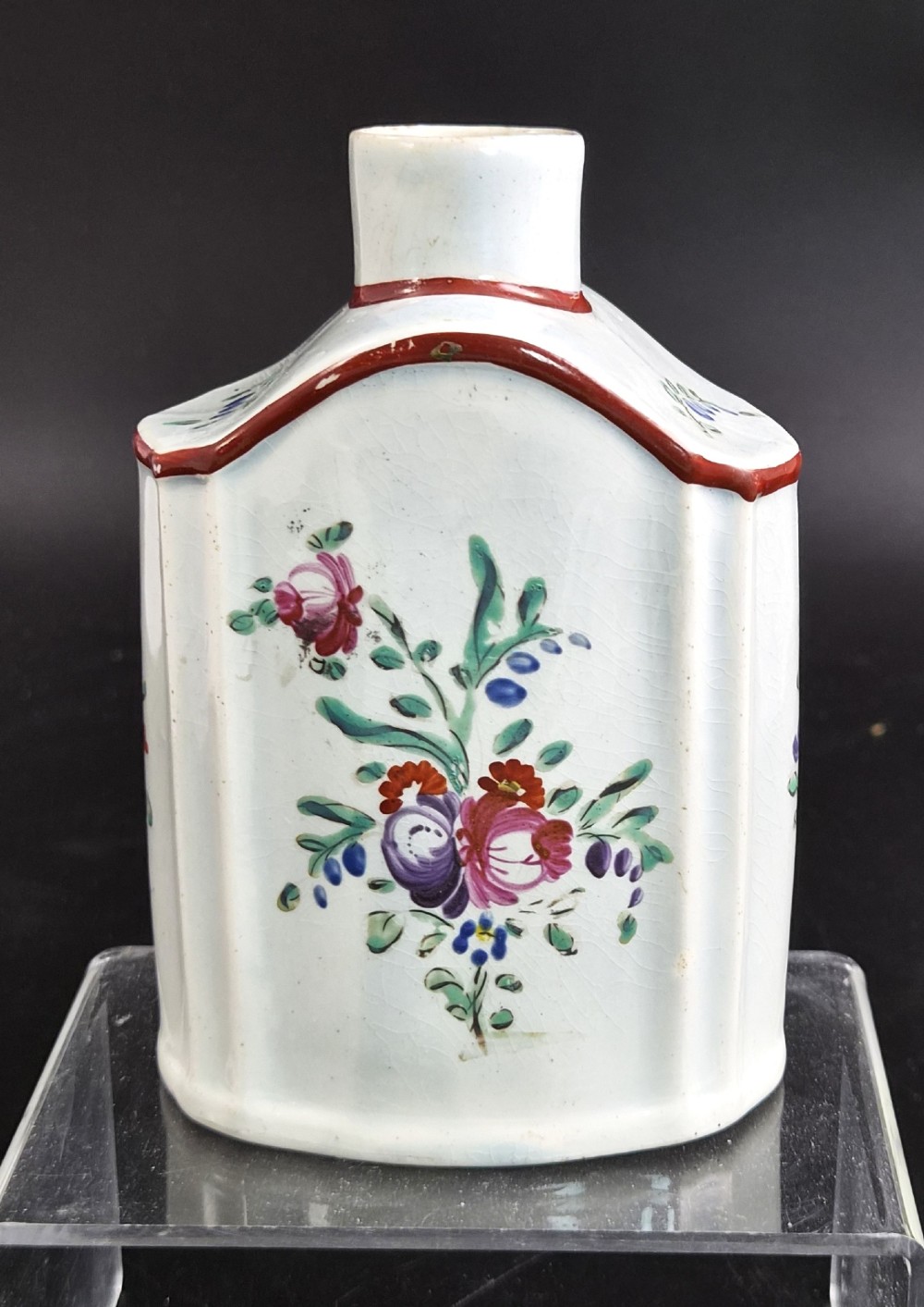 An eighteenth-century creamware tea canister with hand-painted floral enamel motifs in purple, red, and green on an off-white earthenware body with arched reddish-brown shoulders.