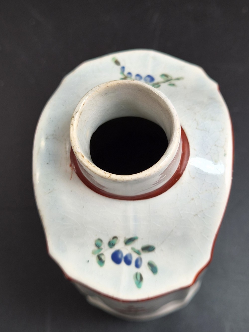 An eighteenth-century creamware tea canister with hand-painted floral enamel motifs in purple, red, and green on an off-white earthenware body with arched reddish-brown shoulders. View V