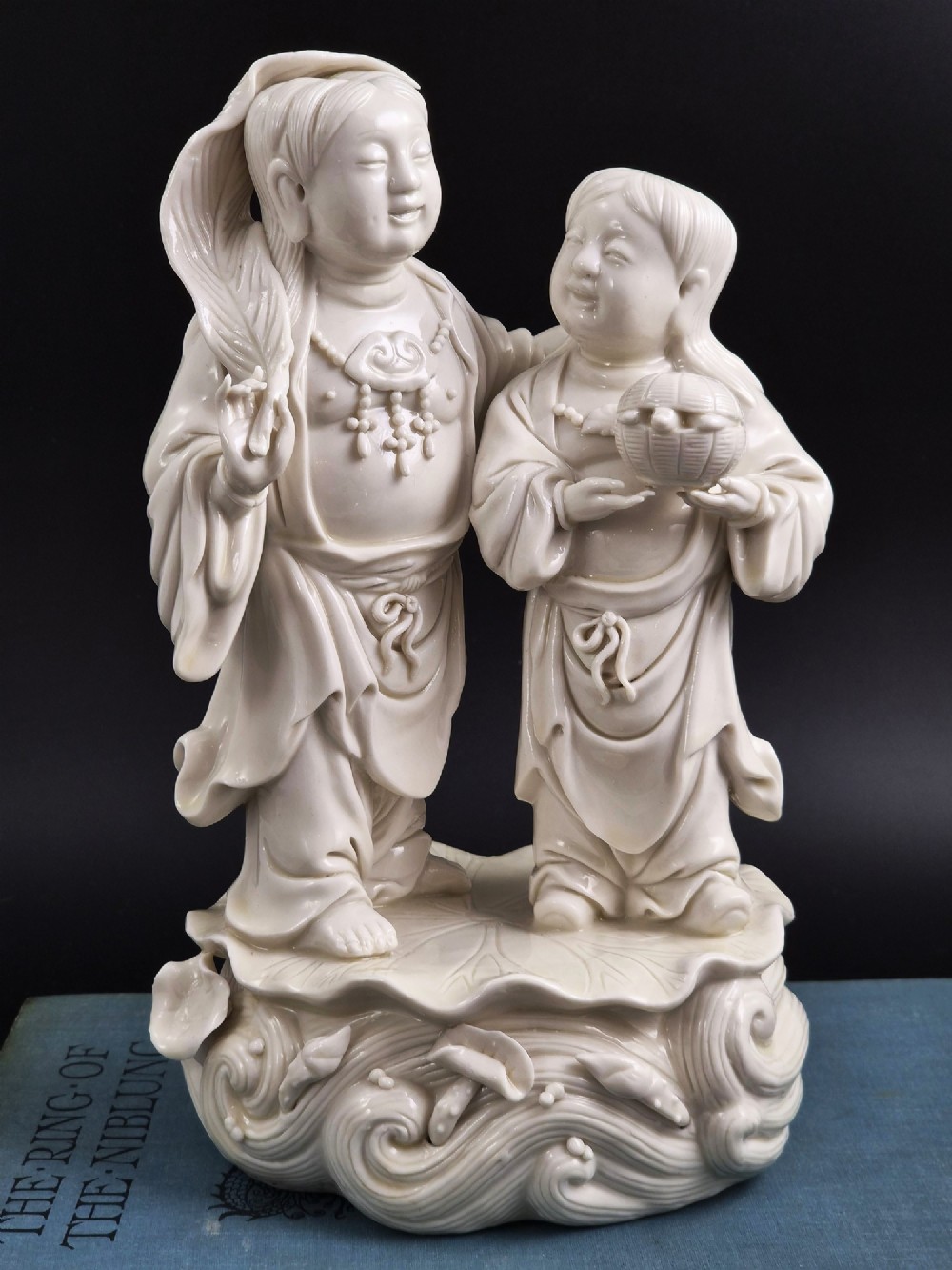A Qing Dynasty Blanc-de-Chine white porcelain figure group depicting the Hehe Erxian standing on a stylised lotus and wave base. View III