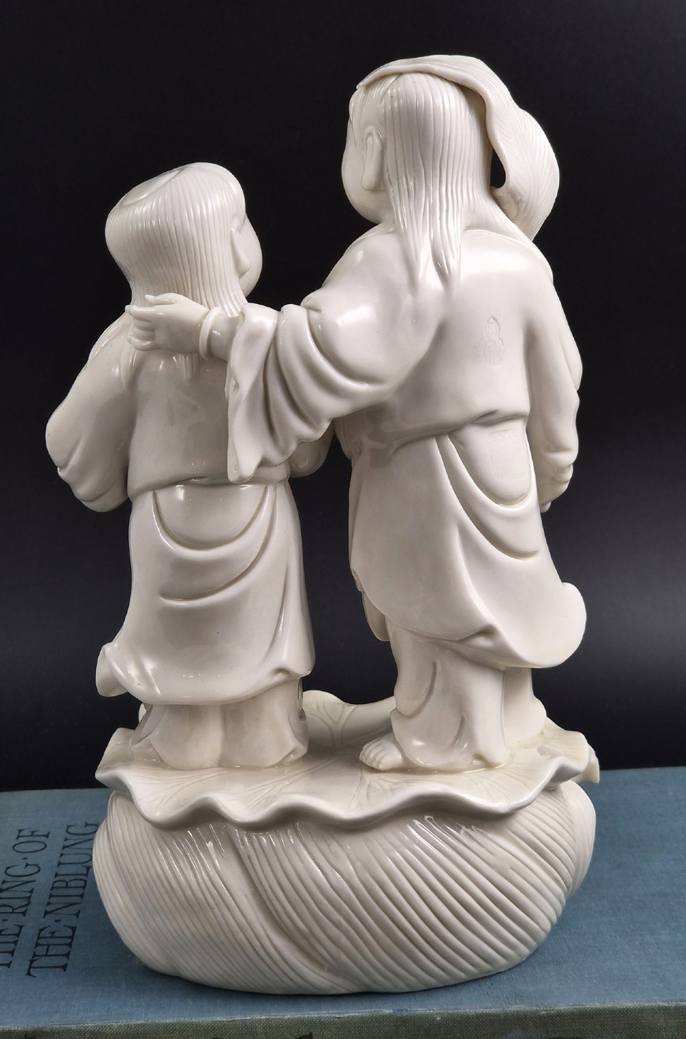 A Qing Dynasty Blanc-de-Chine white porcelain figure group depicting the Hehe Erxian standing on a stylised lotus and wave base. View VI