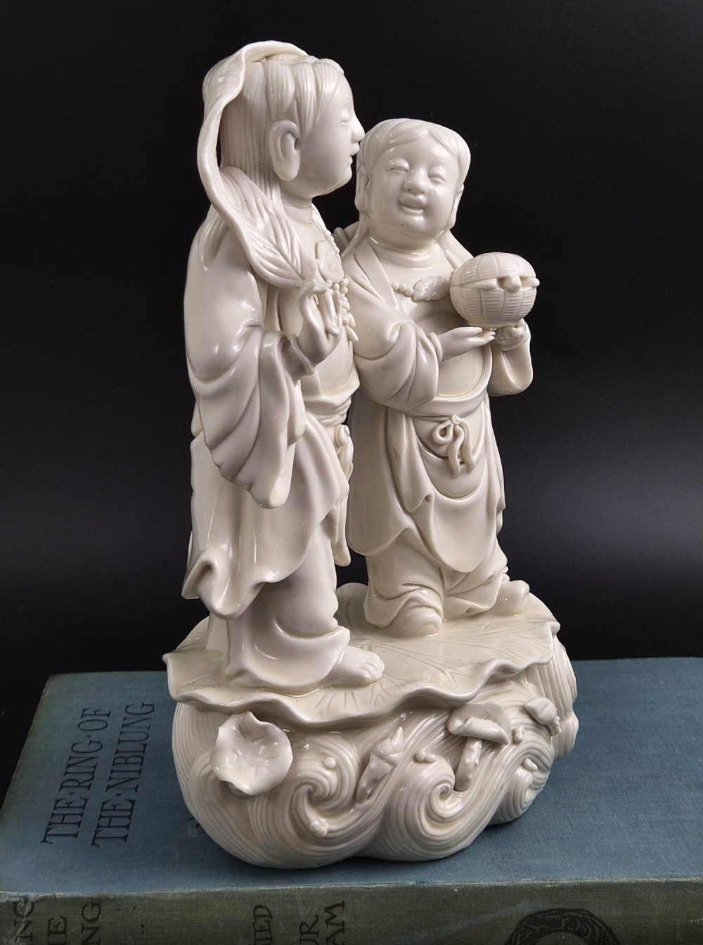A Qing Dynasty Blanc-de-Chine white porcelain figure group depicting the Hehe Erxian standing on a stylised lotus and wave base. View VIII