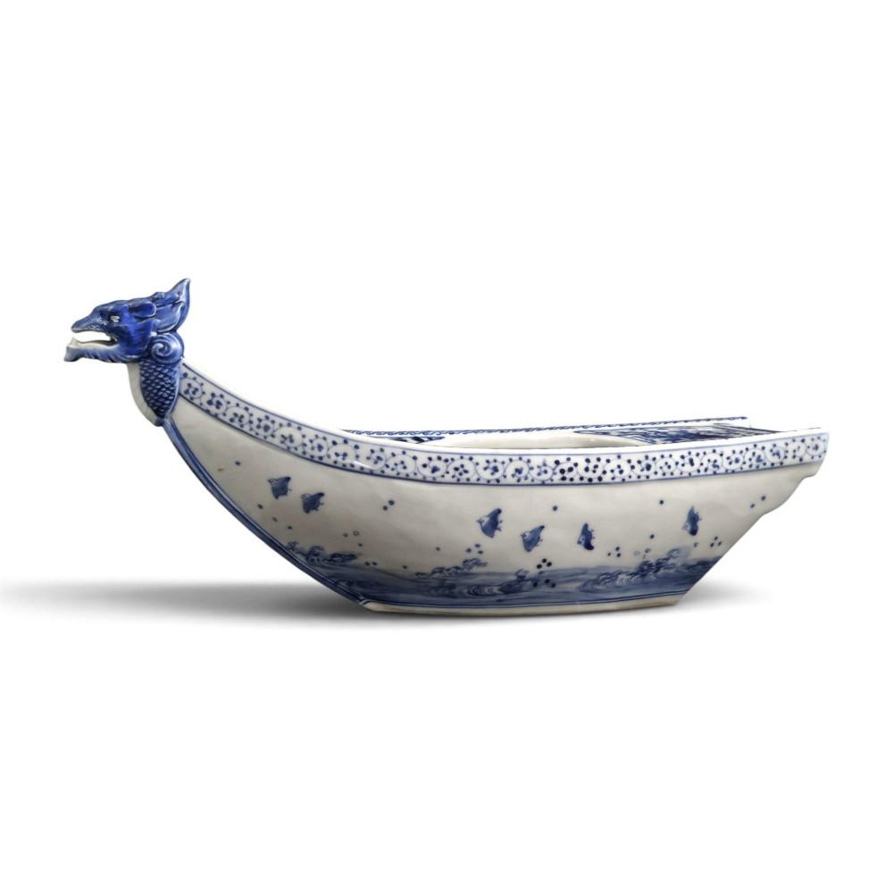 A Japanese blue and white porcelain vessel shaped like a boat featuring a carved dragon figurehead at the prow. View V