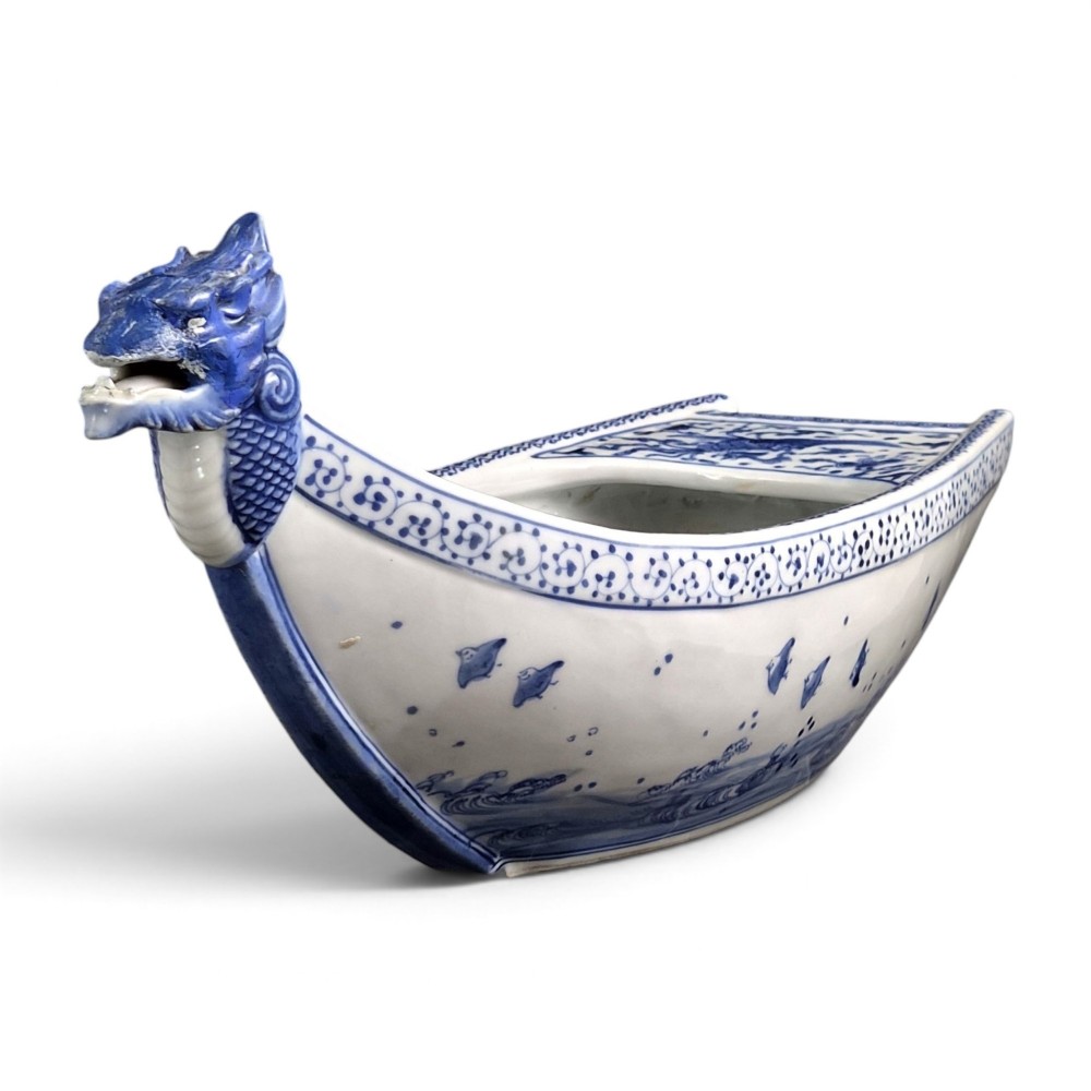 A Japanese blue and white porcelain vessel shaped like a boat featuring a carved dragon figurehead at the prow. View VI