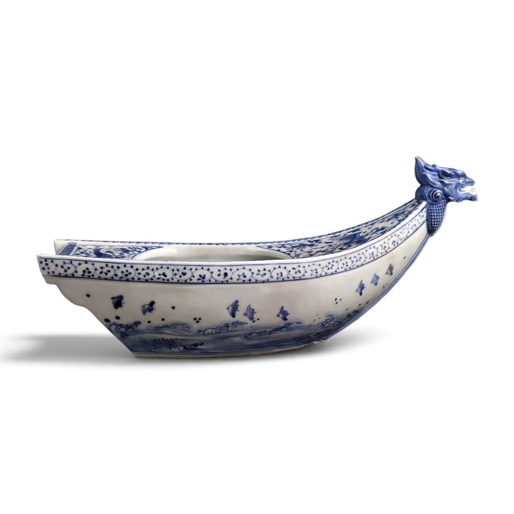 A Japanese blue and white porcelain vessel shaped like a boat featuring a carved dragon figurehead at the prow. View VII