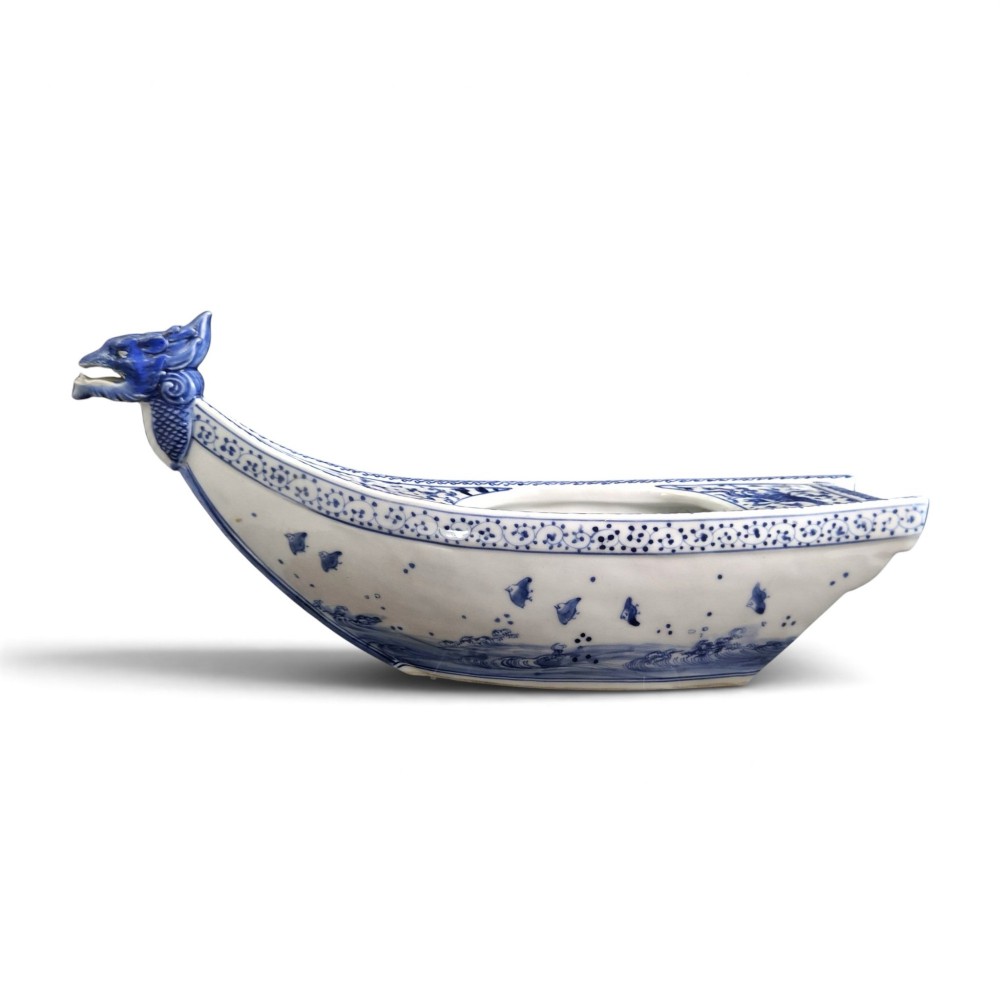 A Japanese blue and white porcelain vessel shaped like a boat featuring a carved dragon figurehead at the prow. View X
