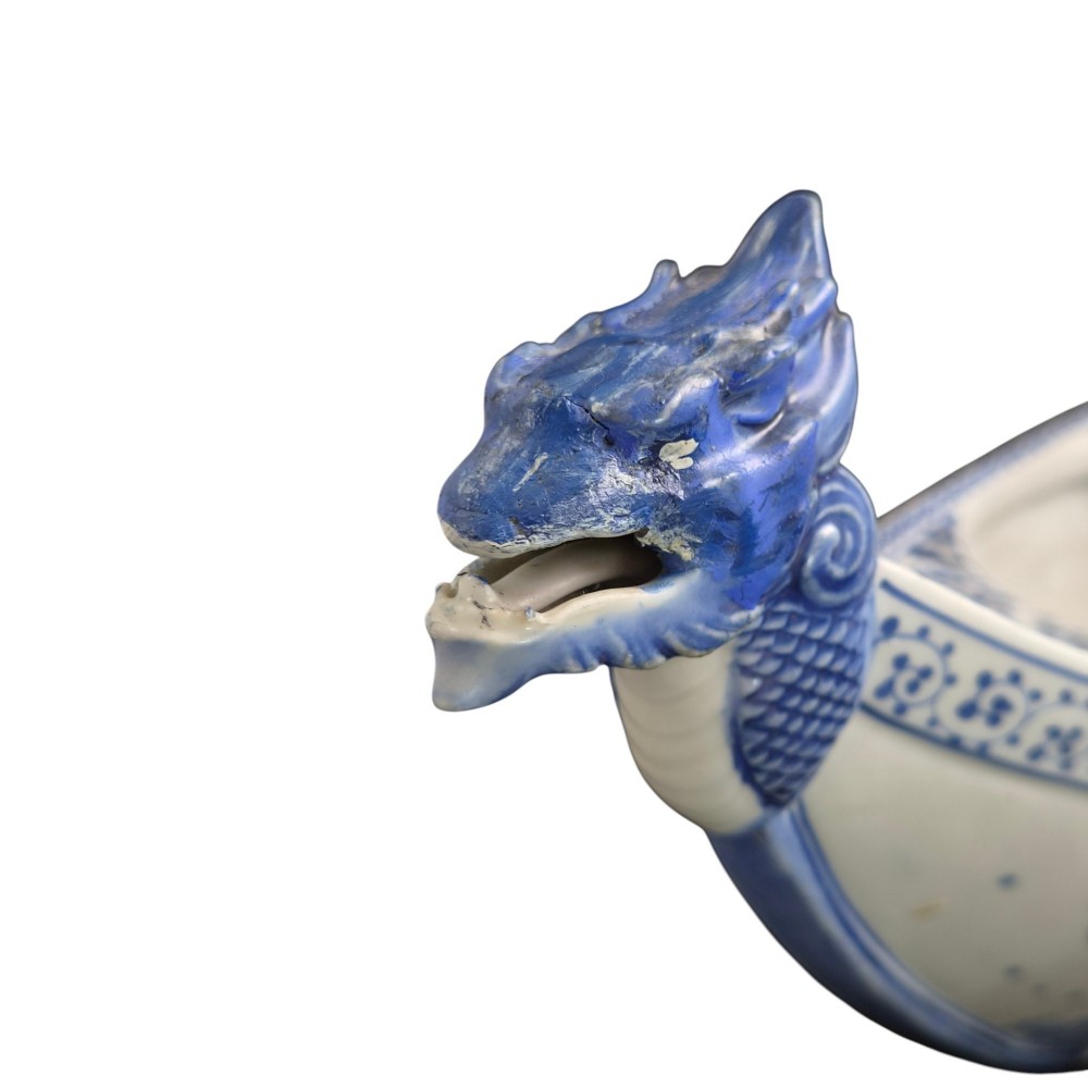 A Japanese blue and white porcelain vessel shaped like a boat featuring a carved dragon figurehead at the prow. View XII