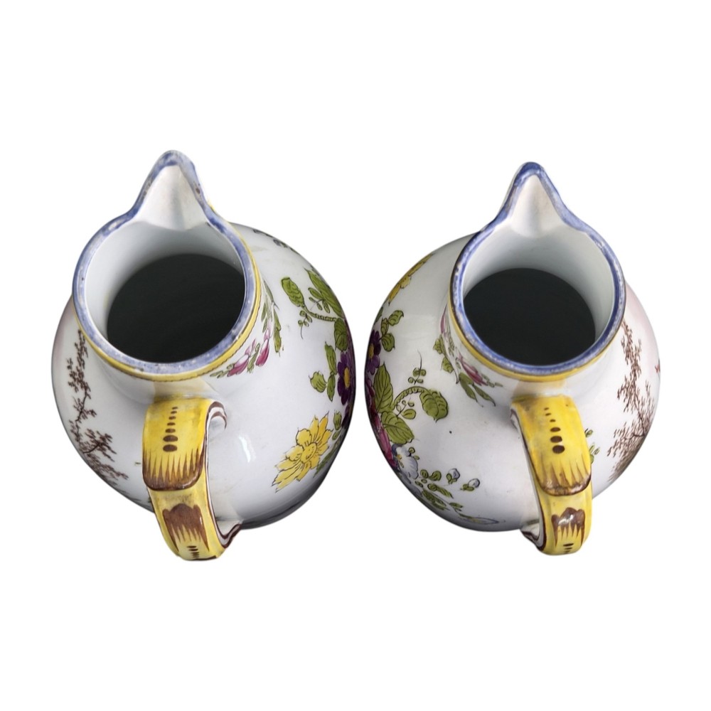A pair of 18th-century white tin-glazed earthenware oil and vinegar jugs decorated with hand-painted floral motifs and fitted with yellow finial covers. View V
