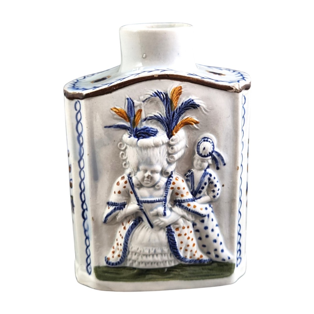 An 18th-century Prattware earthenware tea canister featuring relief-moulded depictions of two Georgian Macaroni figures in blue, ochre, and green underglaze glazes against an off-white background. View II