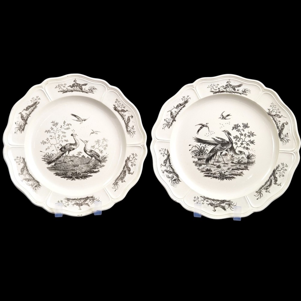 A pair of round cream-coloured earthenware plates featuring monochrome transfer prints of birds and moulded scalloped rims.