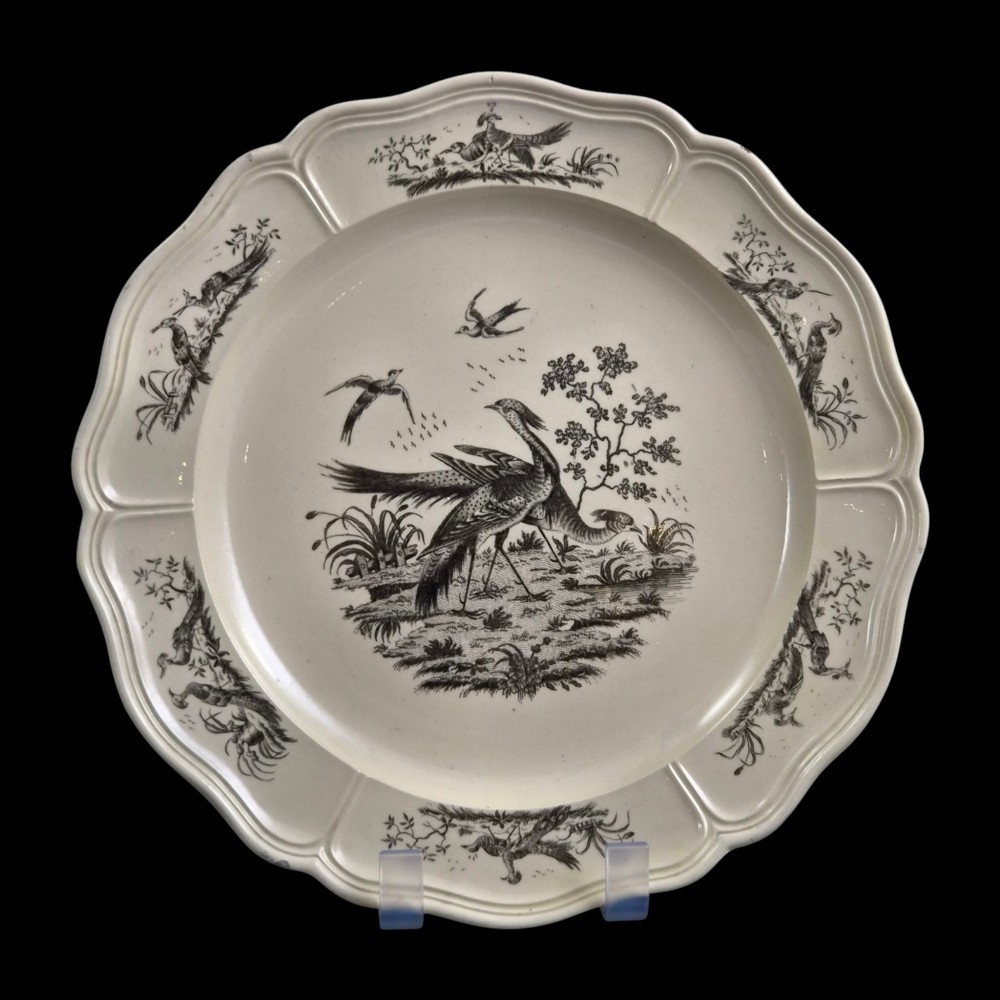 A pair of round cream-coloured earthenware plates featuring monochrome transfer prints of birds and moulded scalloped rims. View III